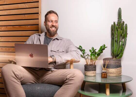 Kollege am Schreibtisch mit Laptop, daneben Pflanzen