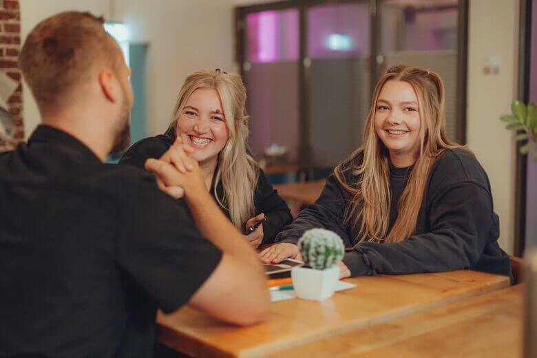 Zwei Kolleginnen lachen bei der Arbeit am Tisch